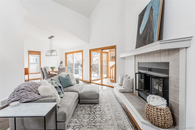 living room with high vaulted ceiling, baseboards, a tiled fireplace, and wood finished floors