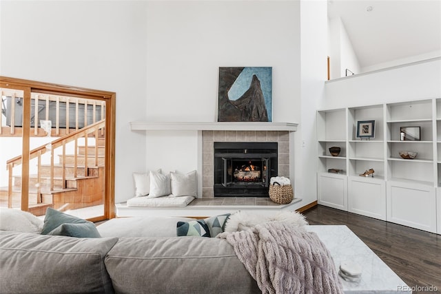 living area with stairway, dark wood-style flooring, a fireplace, and a towering ceiling