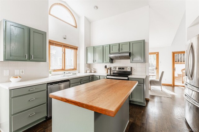 kitchen with high vaulted ceiling, under cabinet range hood, green cabinets, appliances with stainless steel finishes, and tasteful backsplash