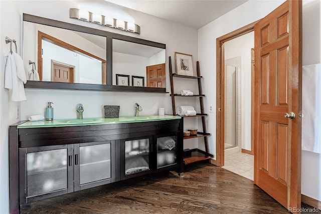 full bathroom featuring double vanity, a shower stall, a sink, and wood finished floors