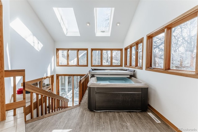 misc room featuring vaulted ceiling with skylight, visible vents, baseboards, and wood finished floors