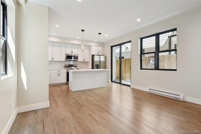 1563 N Hooker St, Denver, CO 80204 - kitchen featuring appliances with stainless steel finishes, baseboard heating, white cabinets, a kitchen island, and backsplash