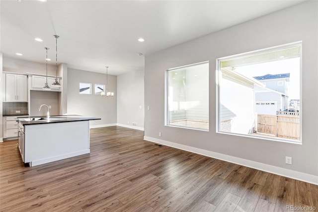 kitchen featuring white cabinetry, tasteful backsplash, an island with sink, dark wood-type flooring, and pendant lighting