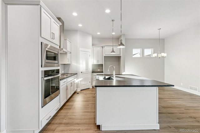 kitchen with white cabinets, appliances with stainless steel finishes, sink, and a kitchen island with sink