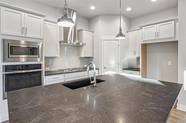 kitchen with dark stone counters, white cabinets, hanging light fixtures, sink, and appliances with stainless steel finishes