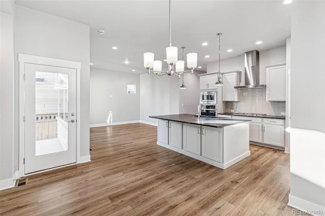 kitchen featuring stainless steel appliances, light hardwood / wood-style floors, pendant lighting, wall chimney range hood, and white cabinetry