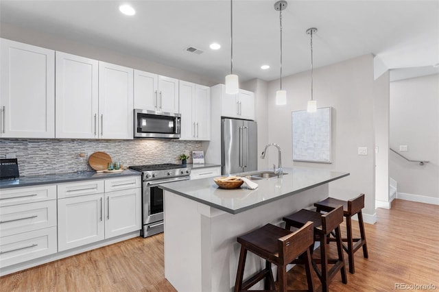 kitchen featuring sink, hanging light fixtures, stainless steel appliances, a kitchen island with sink, and white cabinets