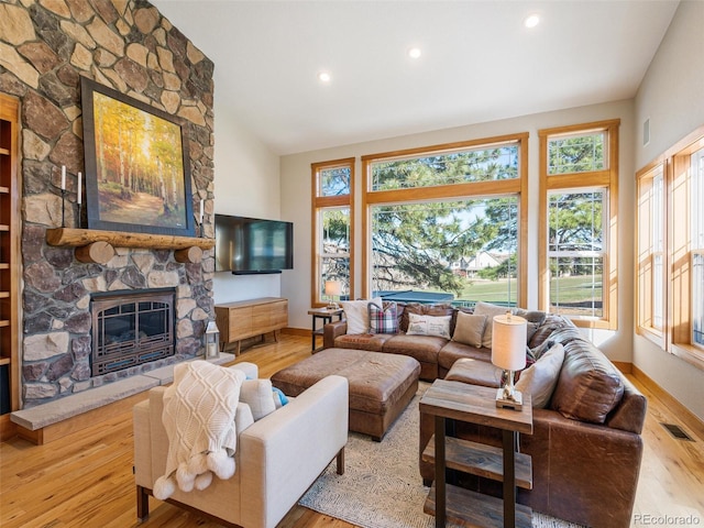 living area featuring visible vents, baseboards, a stone fireplace, and wood finished floors