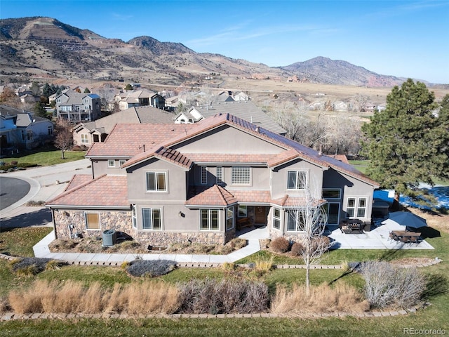 back of property with a chimney, stucco siding, stone siding, a patio area, and a mountain view