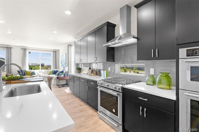 22374 E 49th Pl, Aurora, CO 80019 - kitchen with wall chimney exhaust hood, stainless steel appliances, dark cabinetry, light countertops, and open floor plan