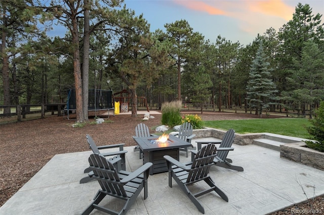 patio terrace at dusk with a lawn, a fire pit, a playground, and a trampoline