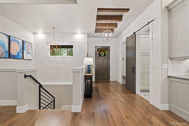 entrance foyer with a notable chandelier, beamed ceiling, light wood-style floors, and a barn door