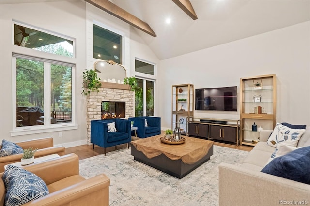 living room with a healthy amount of sunlight, a stone fireplace, beam ceiling, and light hardwood / wood-style floors