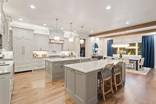 kitchen featuring a kitchen bar, light wood-style flooring, gray cabinets, a large island with sink, and hanging light fixtures