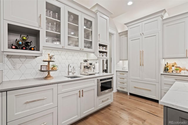 kitchen with backsplash, oven, light hardwood / wood-style flooring, light stone countertops, and sink