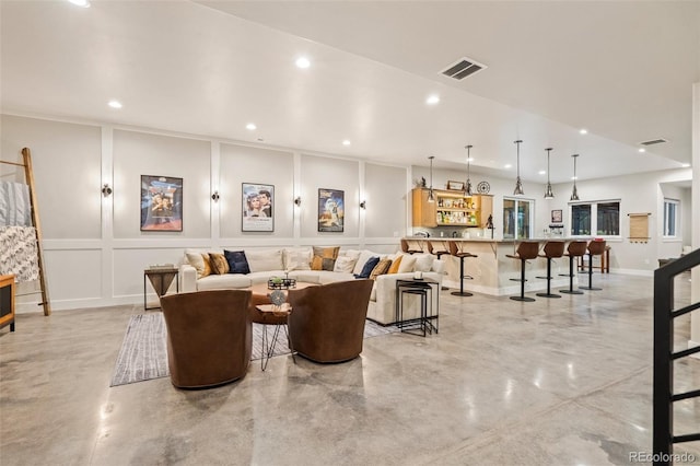 living area featuring recessed lighting, visible vents, finished concrete floors, and a decorative wall