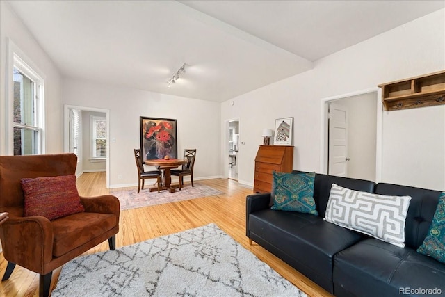 living room with light wood-type flooring, rail lighting, baseboards, and arched walkways