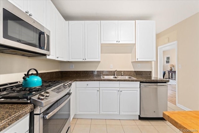 kitchen featuring stainless steel appliances, a sink, dark countertops, white cabinets, and light tile patterned floors