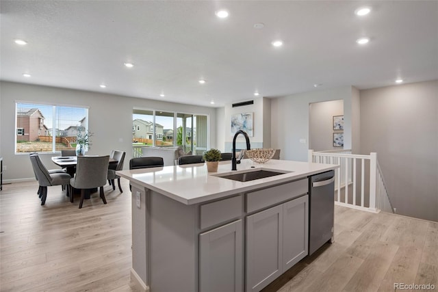 kitchen with an island with sink, dishwasher, gray cabinets, sink, and light hardwood / wood-style floors