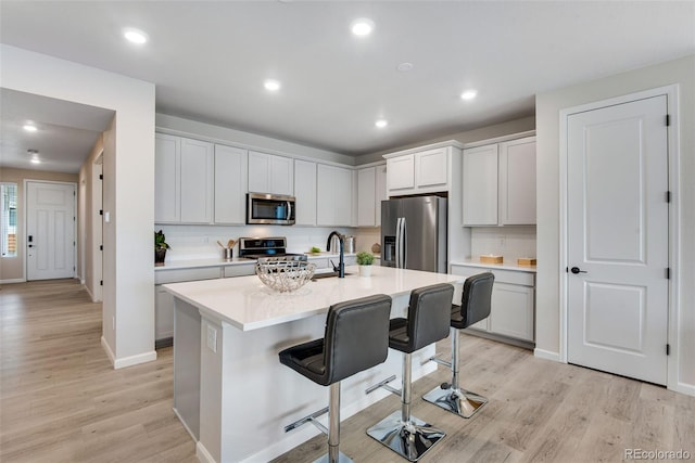 kitchen featuring appliances with stainless steel finishes, light hardwood / wood-style flooring, a breakfast bar area, and an island with sink