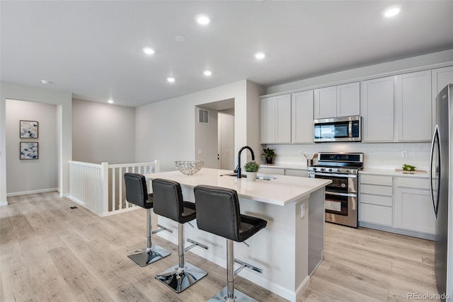 kitchen with a center island with sink, a kitchen breakfast bar, light hardwood / wood-style flooring, sink, and stainless steel appliances