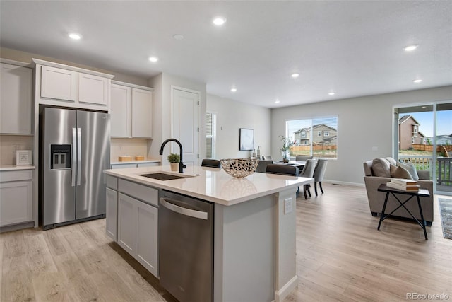 kitchen with light hardwood / wood-style flooring, a kitchen island with sink, stainless steel appliances, and tasteful backsplash