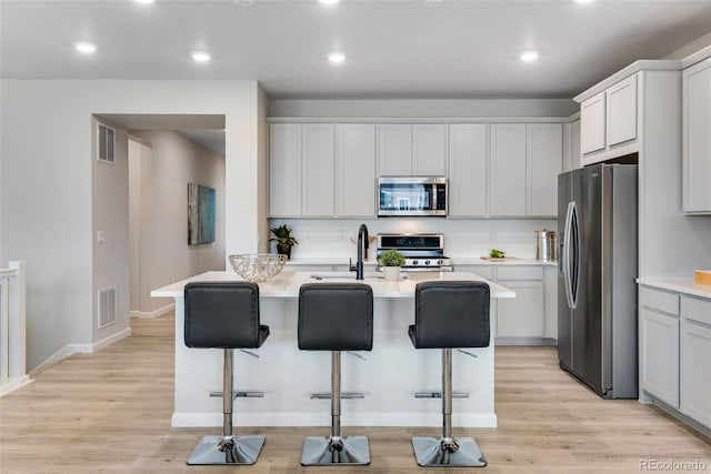 kitchen with appliances with stainless steel finishes, light hardwood / wood-style flooring, a breakfast bar area, and white cabinets