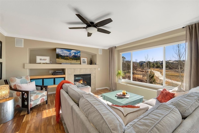 living room featuring ceiling fan, a tiled fireplace, crown molding, and wood-type flooring