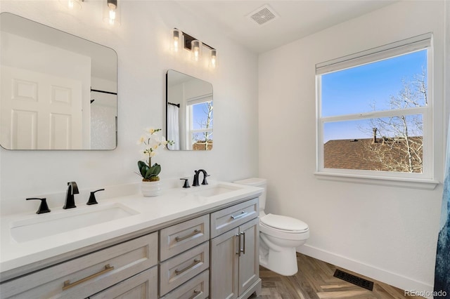 bathroom featuring toilet, parquet floors, vanity, and a wealth of natural light