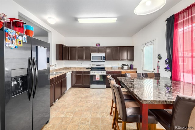 kitchen with dark brown cabinets, appliances with stainless steel finishes, dark stone counters, and sink