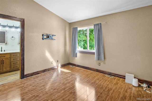 unfurnished bedroom featuring connected bathroom, lofted ceiling, light hardwood / wood-style floors, and sink