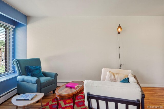 living area with a baseboard radiator, wood finished floors, and baseboards