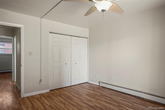 unfurnished bedroom with a closet, baseboard heating, a baseboard heating unit, wood finished floors, and baseboards