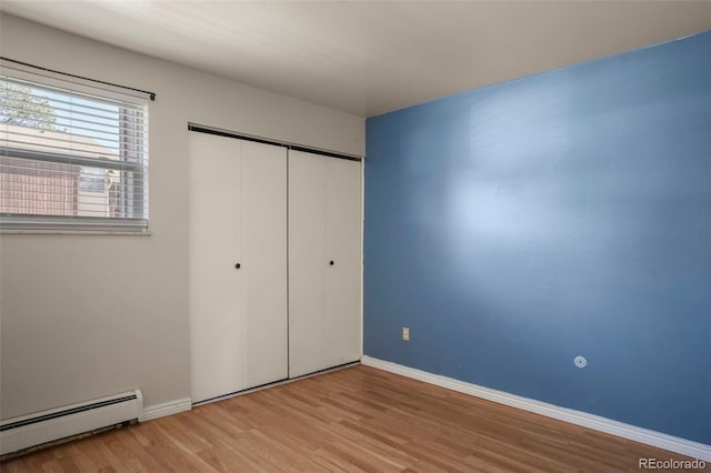 unfurnished bedroom featuring a baseboard heating unit, a closet, baseboards, and light wood-style floors