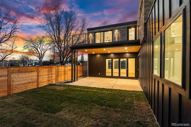 back house at dusk with a balcony, a yard, and a patio