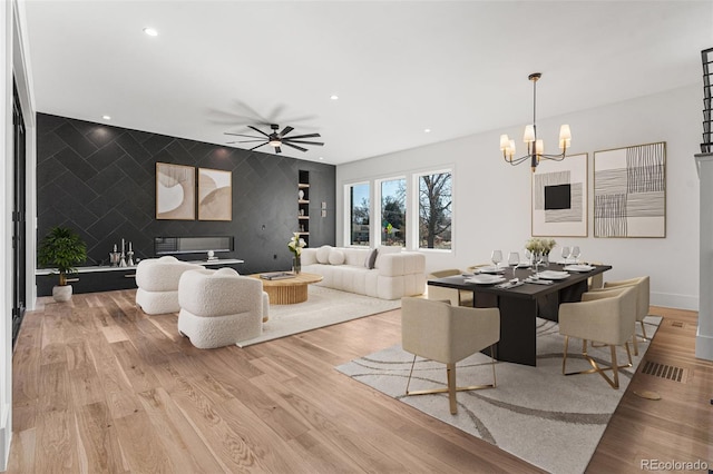 living room with ceiling fan with notable chandelier, light hardwood / wood-style floors, and tile walls