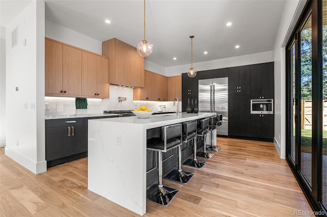 kitchen with sink, hanging light fixtures, light wood-type flooring, a kitchen breakfast bar, and a kitchen island with sink