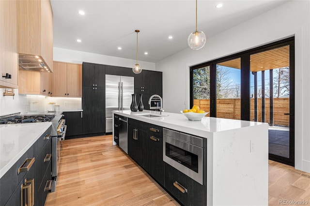 kitchen with light brown cabinets, sink, hanging light fixtures, an island with sink, and high quality appliances