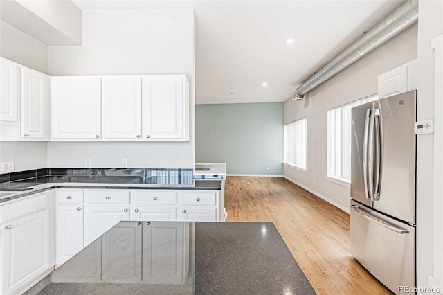 kitchen featuring white cabinetry, dark stone counters, stainless steel refrigerator, and light hardwood / wood-style floors