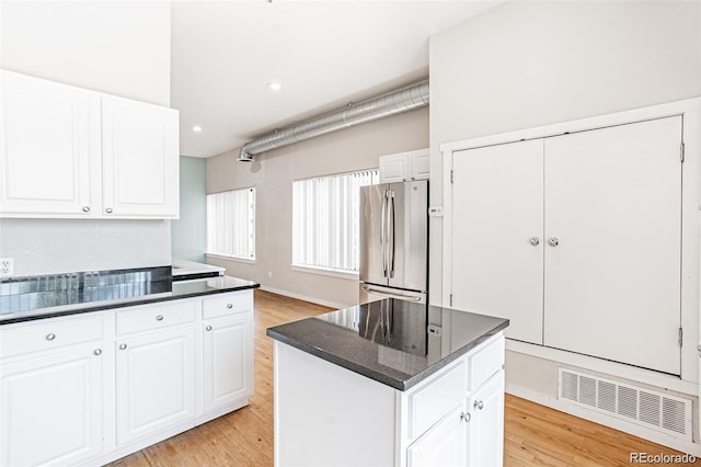 kitchen with white cabinetry, light hardwood / wood-style flooring, stainless steel refrigerator, and a kitchen island