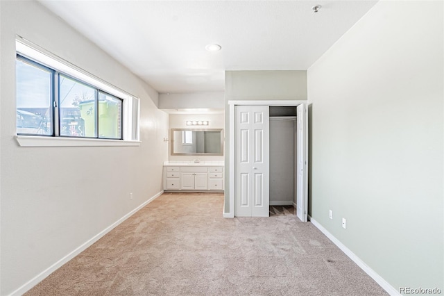 unfurnished bedroom featuring sink, light colored carpet, ensuite bath, and a closet