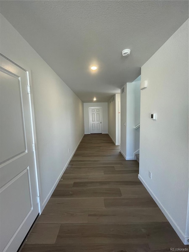 hall with visible vents, a textured ceiling, baseboards, and wood finished floors