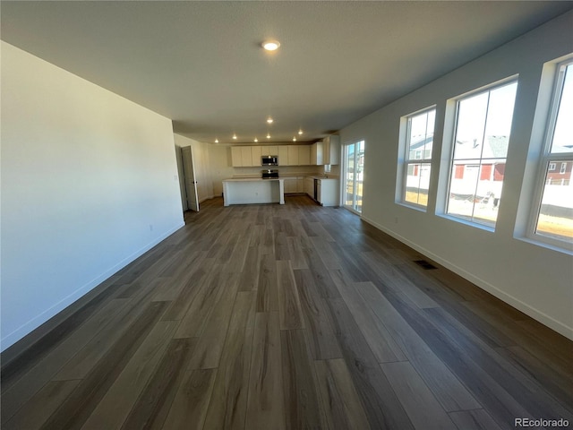 unfurnished living room with visible vents, baseboards, and dark wood-style flooring