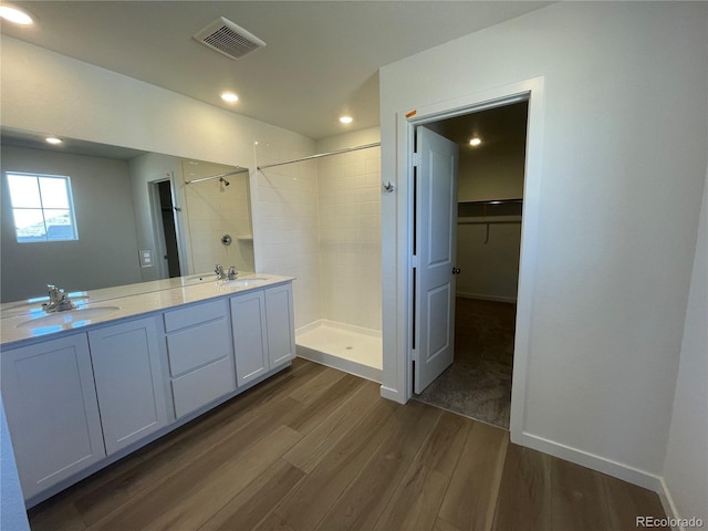 bathroom with a sink, visible vents, wood finished floors, and a tile shower