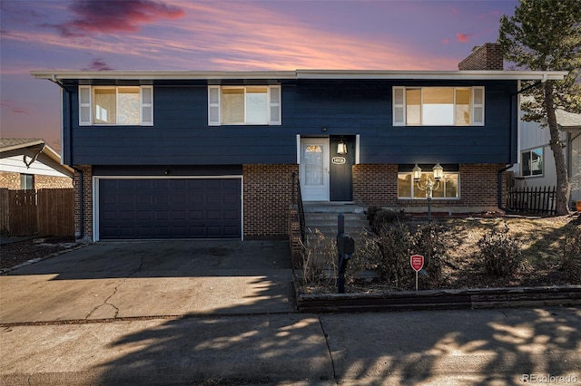 bi-level home with brick siding, a chimney, concrete driveway, an attached garage, and fence