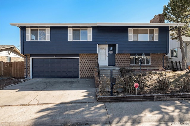 bi-level home with an attached garage, brick siding, fence, driveway, and a chimney