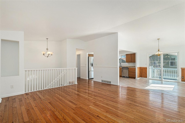 unfurnished living room with light wood-style flooring, vaulted ceiling, visible vents, and a chandelier