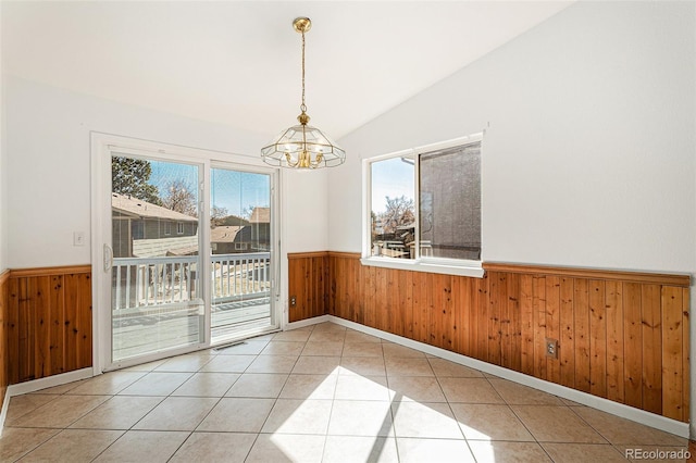 tiled empty room featuring a wainscoted wall, vaulted ceiling, an inviting chandelier, and wooden walls