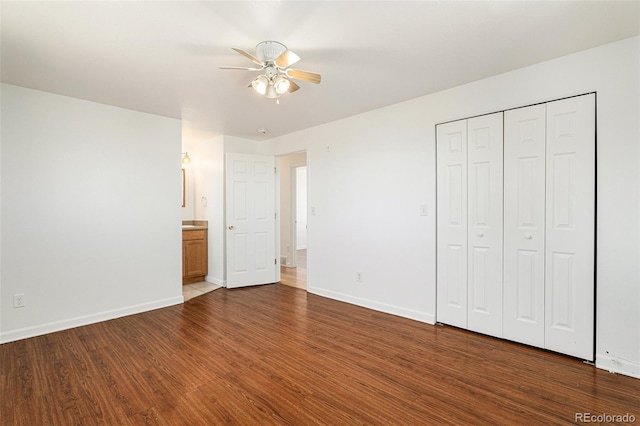 unfurnished bedroom with a closet, ceiling fan, ensuite bath, wood finished floors, and baseboards