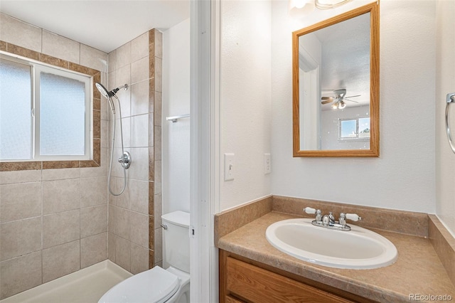 full bath featuring vanity, a tile shower, toilet, and a ceiling fan